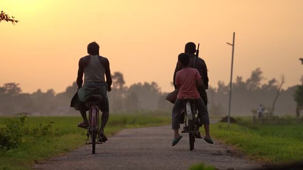 View of people riding bicycles on a rural road at sunset Bangladesh.