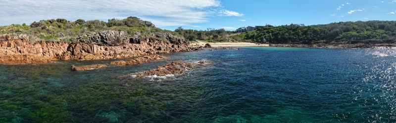 Aerial view of rugged rust colored cliffs meet the turquoise sea near a sandy beach framed by green vegetation Huskisson New South Wales Australia. Aerial view of rugged rust colored cliffs meet the turquoise sea near a sandy beach framed by green vegetation Huskisson New South Wales Australia.