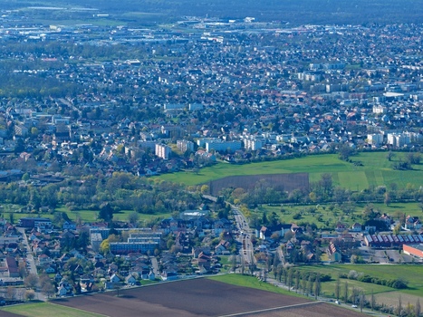 Aerial view of sprawling cityscape meeting verdant fields under a soft diffused light casting long shadows across the landscape Sausheim Grand Est France.