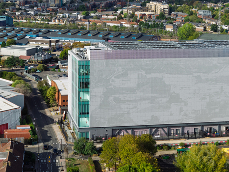 Aerial view of a modern data center building with a large grey facade and glass windows situated in an urban area with surrounding streets and trees in the United Kingdom. Aerial view of a modern data center building with a large grey facade and glass windows situated in an urban area with surrounding streets and trees in the United Kingdom.
