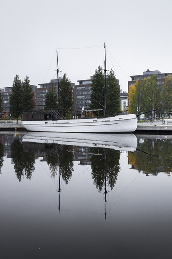 View of a white sailing boat moored at a quay with calm water reflections and modern buildings in the background in Jyvaskyla Central Finland Finland.