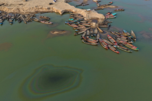 Aerial view of Jadukata River with numerous wooden boats moored along the sandy riverbank featuring an oil slick on the water surface in Sunamganj Sylhet Division Bangladesh. Aerial view of Jadukata River with numerous wooden boats moored along the sandy riverbank featuring an oil slick on the water surface in Sunamganj Sylhet Division Bangladesh.