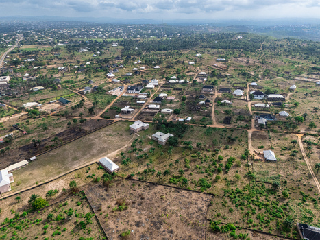 Aerial view of scattered residential buildings and a winding road amidst a tapestry of lush green foliage and warm brown earth under a cloudy sky Elu Abia Nigeria. Aerial view of scattered residential buildings and a winding road amidst a tapestry of lush green foliage and warm brown earth under a cloudy sky Elu Abia Nigeria.