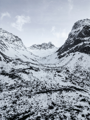 Aerial view of Grotfjord valley with snow covered mountain peaks and rocky slopes under a cloudy winter sky in Tromvik Troms Norway. Aerial view of Grotfjord valley with snow covered mountain peaks and rocky slopes under a cloudy winter sky in Tromvik Troms Norway.