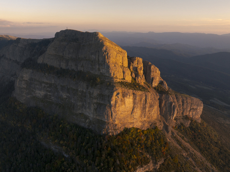 Aerial view of the Pyrenees mountain range at golden hour showcasing rugged cliffs rocky peaks and dense forest slopes under a soft sunset sky in Spain. Aerial view of the Pyrenees mountain range at golden hour showcasing rugged cliffs rocky peaks and dense forest slopes under a soft sunset sky in Spain.