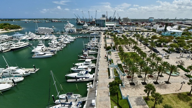 Aerial view of a marina filled with luxury yachts and a palm lined promenade next to a commercial port with cranes in Palm Beach County Florida United States.