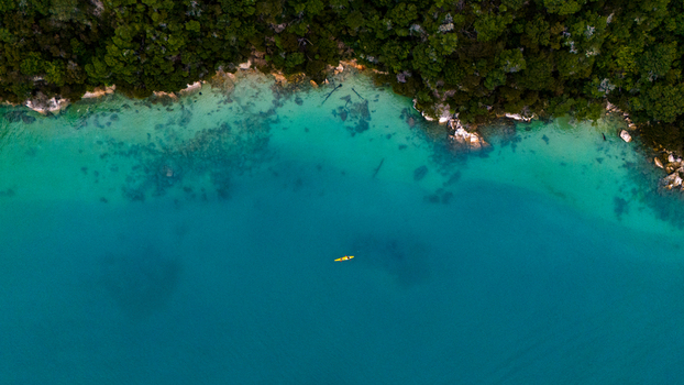 Aerial view of a lone kayak glides through the turquoise waters near the rugged coastline and lush forests of Abel Tasman National Park Abel Tasman National Park New Zealand. Aerial view of a lone kayak glides through the turquoise waters near the rugged coastline and lush forests of Abel Tasman National Park Abel Tasman National Park New Zealand.