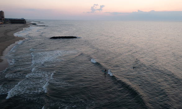 Aerial view of Asbury Park Beach at sunset with gentle waves rolling onto the sandy shore and a surfer in the water Asbury Park New Jersey United States.