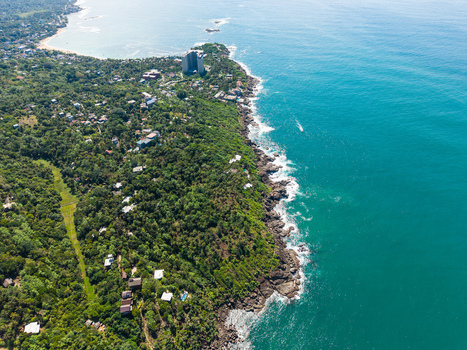 Aerial view of the lush tropical coastline with rocky cliffs meeting the turquoise ocean water and scattered buildings among dense greenery in Galle Southern Province Sri Lanka. Aerial view of the lush tropical coastline with rocky cliffs meeting the turquoise ocean water and scattered buildings among dense greenery in Galle Southern Province Sri Lanka.