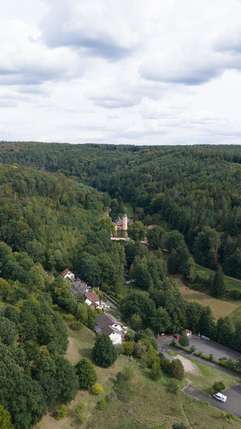 Aerial view of Schloss Mespelbrunn nestled in a lush green valley surrounded by dense forests and rolling hills in Mespelbrunn Bayern Germany. Aerial view of Schloss Mespelbrunn nestled in a lush green valley surrounded by dense forests and rolling hills in Mespelbrunn Bayern Germany.