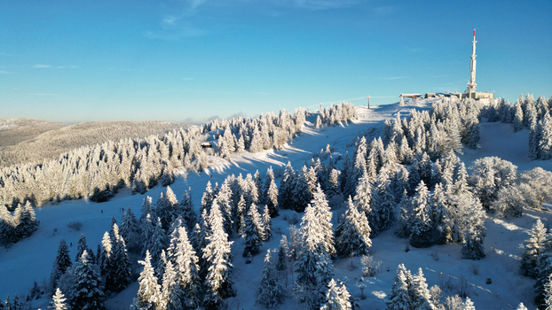 Aerial view of the snow covered slopes and pine forests of Col de la Faucille with a radio tower on the mountain peak in Gex Auvergne Rhone Alpes France. Aerial view of the snow covered slopes and pine forests of Col de la Faucille with a radio tower on the mountain peak in Gex Auvergne Rhone Alpes France.