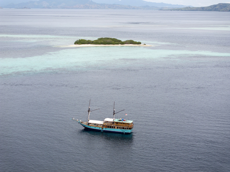 Aerial view of a traditional wooden phinisi boat sailing through the turquoise waters near a small island in Komodo East Nusa Tenggara Indonesia.