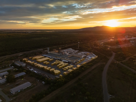 Aerial view of an industrial logistics yard with stacked yellow containers factory buildings and rail tracks beside wooded countryside at sunset in Visonta Hungary.