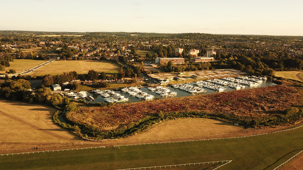 Aerial view of a marina filled with boats surrounded by fields trees and residential buildings under a warm sunset light in Windsor England United Kingdom. Aerial view of a marina filled with boats surrounded by fields trees and residential buildings under a warm sunset light in Windsor England United Kingdom.