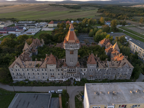 Aerial view of the historic Hajmasker Barracks featuring a prominent central tower weathered red tiled roofs and overgrown courtyards in Hajmasker Hungary. Aerial view of the historic Hajmasker Barracks featuring a prominent central tower weathered red tiled roofs and overgrown courtyards in Hajmasker Hungary.