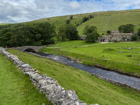View of a stone bridge over a flowing river and a traditional stone farmhouse surrounded by green hills and dry stone walls Hawes England United Kingdom. View of a stone bridge over a flowing river and a traditional stone farmhouse surrounded by green hills and dry stone walls Hawes England United Kingdom.
