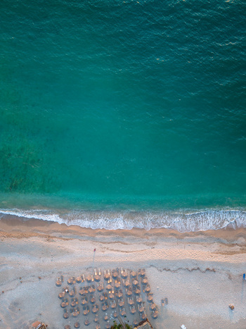Aerial view of a pristine beach with turquoise water white sand and rows of beach umbrellas in Albania.