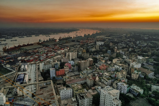 Chattogram Bangladesh 06 January 2022 Aerial view of the busy Chattogram port area with cargo ships shipping containers and the dense urban cityscape under a golden sunset sky.