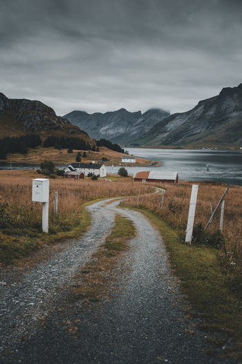 Nordland Norway 09 September 2022 View of a gravel road leading towards traditional houses and a fjord in the Lofoten islands under a cloudy sky. Nordland Norway 09 September 2022 View of a gravel road leading towards traditional houses and a fjord in the Lofoten islands under a cloudy sky.
