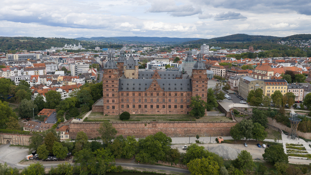 Aerial view of Schloss Johannisburg a historic red sandstone palace surrounded by the cityscape lush trees and a cloudy sky in Aschaffenburg Bayern Germany.