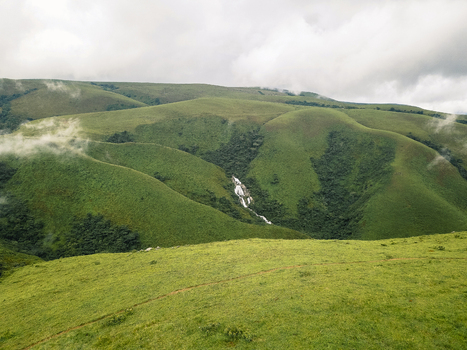 Aerial view of lush green rolling hills a white waterfall plunging into a deep valley clouds on peaks Obudu Cross River Nigeria.