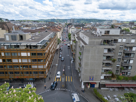 Aerial view of a busy urban street with modern architecture parked cars and distant green hills under a cloudy sky in Biel Bienne Canton of Bern Switzerland. Aerial view of a busy urban street with modern architecture parked cars and distant green hills under a cloudy sky in Biel Bienne Canton of Bern Switzerland.
