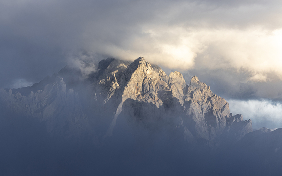 View of a rugged mountain peak piercing through a sea of swirling clouds bathed in golden sunlight Picos de Europa Asturias Spain. View of a rugged mountain peak piercing through a sea of swirling clouds bathed in golden sunlight Picos de Europa Asturias Spain.