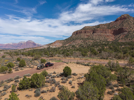 Aerial view of an SUV pulling a teardrop camper trailer on a dirt road at Gooseberry Mesa with the red rock landscape of Zion National Park in Hurricane Utah United States. Aerial view of an SUV pulling a teardrop camper trailer on a dirt road at Gooseberry Mesa with the red rock landscape of Zion National Park in Hurricane Utah United States.