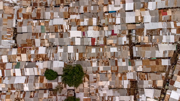 Aerial view of a dense urban neighborhood featuring a patchwork of corrugated metal rooftops in various states of rust and wear with green trees Tamale Northern Region Ghana. Aerial view of a dense urban neighborhood featuring a patchwork of corrugated metal rooftops in various states of rust and wear with green trees Tamale Northern Region Ghana.