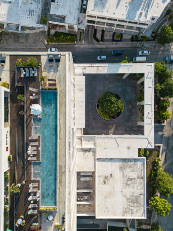 Aerial view of a modern building featuring a long rectangular swimming pool a circular courtyard with a tree and surrounding urban streets in Merida Yucatan Mexico. Aerial view of a modern building featuring a long rectangular swimming pool a circular courtyard with a tree and surrounding urban streets in Merida Yucatan Mexico.