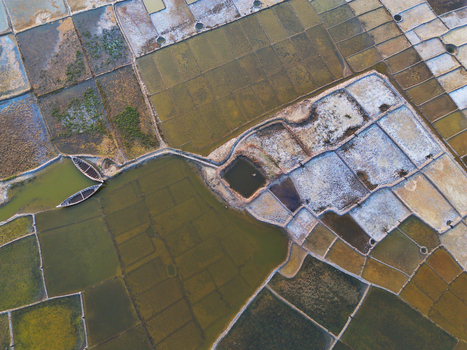 Aerial view of geometric salt pans with varying water levels and two traditional wooden boats in a narrow waterway in Moheskhali Upazila Chittagong Division Bangladesh. Aerial view of geometric salt pans with varying water levels and two traditional wooden boats in a narrow waterway in Moheskhali Upazila Chittagong Division Bangladesh.