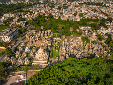 Aerial view of the historic Ahar Cenotaphs with numerous stone domes and monuments surrounded by lush green trees and the urban cityscape of Udaipur Rajasthan India.