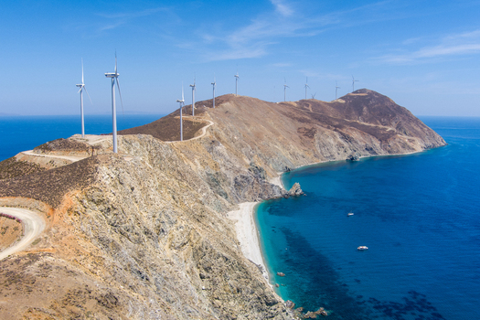 Greece 21 September 2026 Aerial view of wind turbines situated on a rugged coastal ridge overlooking the Aegean Sea with clear blue water and rocky cliffs. Greece 21 September 2026 Aerial view of wind turbines situated on a rugged coastal ridge overlooking the Aegean Sea with clear blue water and rocky cliffs.