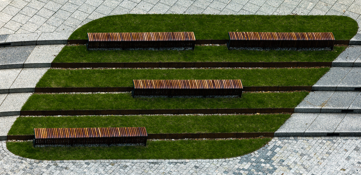 Aerial view of modern wooden slatted benches on green lawn strips within a stone paved urban plaza in Warsaw Masovian Voivodeship Poland.