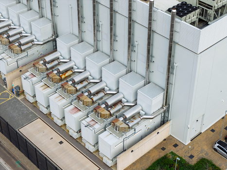 Aerial view of a data center facility featuring multiple cooling units and exhaust pipes mounted on the exterior wall of the industrial building in the United Kingdom.