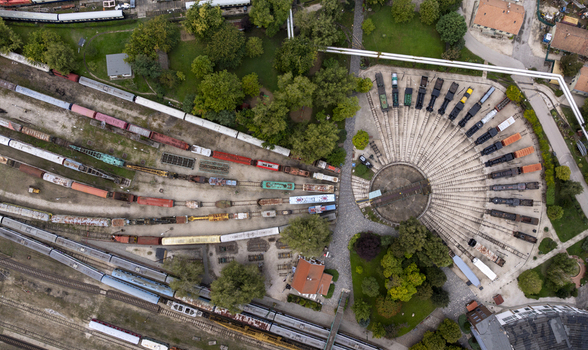 Aerial view of the Hungarian Railway Museum featuring a historic roundhouse with a central turntable and vintage locomotives parked on radiating tracks surrounded by greenery in Budapest Hungary. Aerial view of the Hungarian Railway Museum featuring a historic roundhouse with a central turntable and vintage locomotives parked on radiating tracks surrounded by greenery in Budapest Hungary.