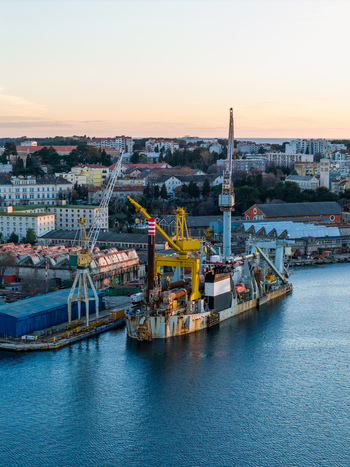 Aerial view of Uljanik Shipyard with industrial cranes and a large vessel docked at the waterfront in Pula Croatia. Aerial view of Uljanik Shipyard with industrial cranes and a large vessel docked at the waterfront in Pula Croatia.