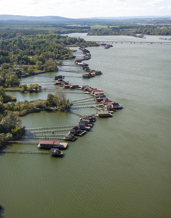 Aerial view of Bokodi Floating Village with its colorful wooden houses built on stilts over the lake surrounded by lush green trees and calm water in Oroszlany Hungary. Aerial view of Bokodi Floating Village with its colorful wooden houses built on stilts over the lake surrounded by lush green trees and calm water in Oroszlany Hungary.