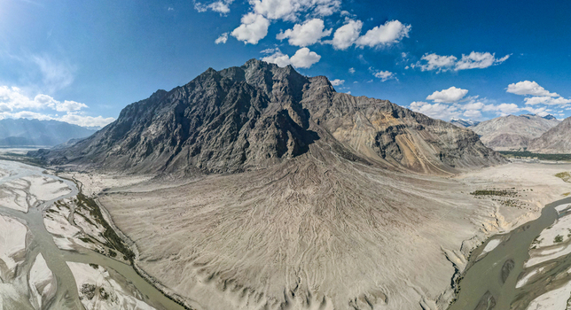Aerial view of Shigar Valley featuring a massive mountain peak rising above a sprawling alluvial fan and the winding river below under a clear blue sky in Shigar Gilgit Pakistan.