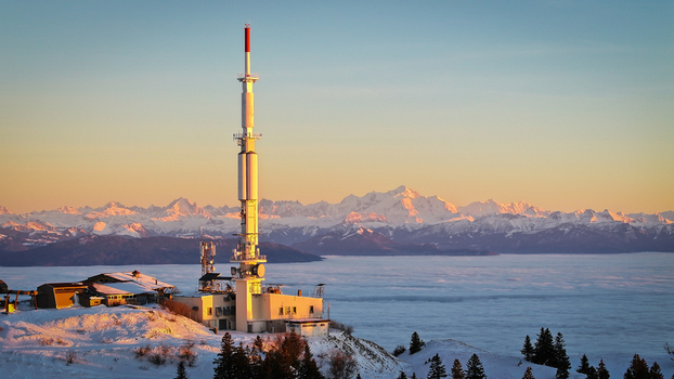 Aerial view of the Mont Blanc massif and a telecommunications tower on a snowy mountain ridge above a sea of clouds during sunset in Chamonix Auvergne Rhone Alpes France. Aerial view of the Mont Blanc massif and a telecommunications tower on a snowy mountain ridge above a sea of clouds during sunset in Chamonix Auvergne Rhone Alpes France.