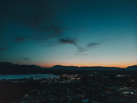 Aerial view of Port Alberni at dusk with glowing city lights mountains in the background and a calm body of water under a twilight sky in Port Alberni British Columbia Canada.