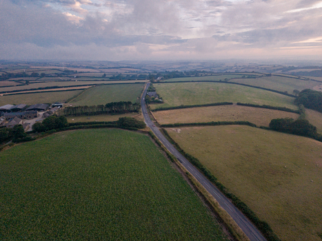 Aerial view of agricultural farmland with hedgerows green fields and a road cutting through the landscape in Looe Cornwall United Kingdom. Aerial view of agricultural farmland with hedgerows green fields and a road cutting through the landscape in Looe Cornwall United Kingdom.