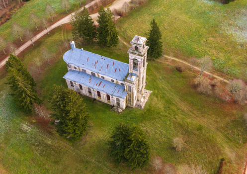 Aerial view of the historic Palendriai church with its white walls and blue roof surrounded by green fields and tall pine trees in Palendriai Siauliu apskritis Lithuania.