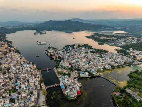 Aerial view of the historic city of Udaipur featuring Lake Pichola the iconic Lake Palace and traditional architecture surrounded by hills at sunset in Udaipur Rajasthan India.