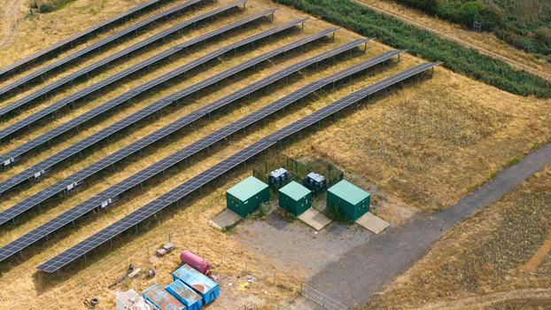 Aerial view of a solar farm with rows of photovoltaic panels green battery storage units and electrical transformers situated in a rural field in Bedford England United Kingdom. Aerial view of a solar farm with rows of photovoltaic panels green battery storage units and electrical transformers situated in a rural field in Bedford England United Kingdom.