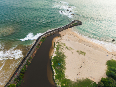 Aerial view of a stone breakwater extending into the turquoise ocean with waves crashing against rocks and a sandy beach Galle Southern Province Sri Lanka.