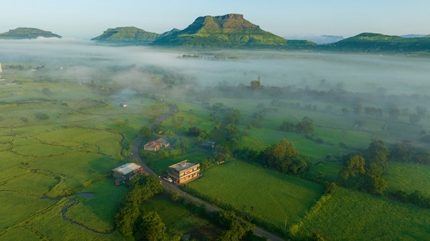 Aerial view of the lush green landscape featuring rolling hills misty valleys and small rural houses along a winding road in Igatpuri Maharashtra India.