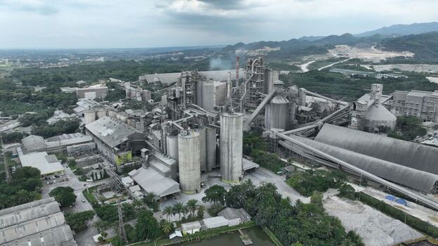 Aerial view of a large industrial cement plant with tall silos complex machinery and conveyor belts surrounded by lush vegetation and hills Klapanunggal West Java Indonesia. Aerial view of a large industrial cement plant with tall silos complex machinery and conveyor belts surrounded by lush vegetation and hills Klapanunggal West Java Indonesia.