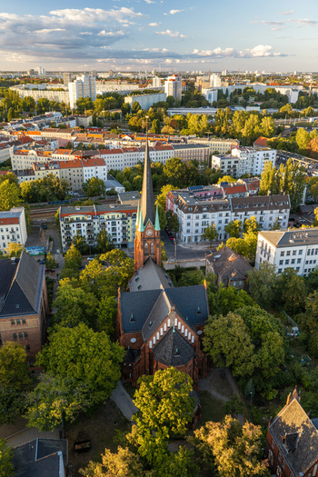 Aerial view of Erloserkirche Church surrounded by lush green trees and urban residential buildings in the Lichtenberg district Berlin Berlin Germany. Aerial view of Erloserkirche Church surrounded by lush green trees and urban residential buildings in the Lichtenberg district Berlin Berlin Germany.