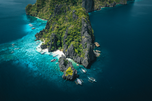 Aerial view of the dramatic limestone cliffs of El Nido surrounded by turquoise waters and traditional outrigger boats anchored near sandy beaches in El Nido Mimaropa Philippines. Aerial view of the dramatic limestone cliffs of El Nido surrounded by turquoise waters and traditional outrigger boats anchored near sandy beaches in El Nido Mimaropa Philippines.